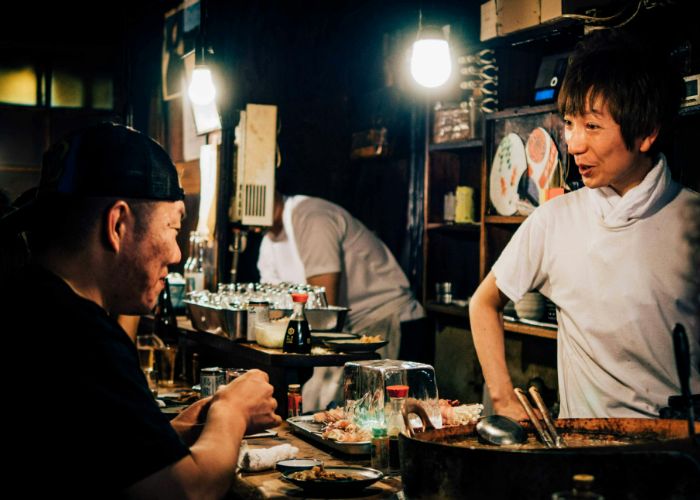 A man speaking to a bartender at a Japanese bar.